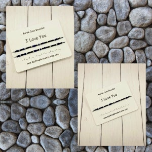Pu&ograve; includere: Due braccialetti di amicizia neri e argentati con il messaggio "Ti amo" in codice Morse. I braccialetti sono esposti su una superficie di legno con sfondo bianco. &Egrave; anche visibile il testo "Braccialetto in codice Morse" e "www.DjsWrapBracelets.etsy.com".