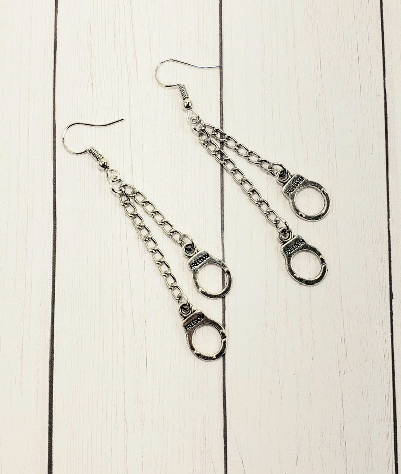 May include: A pair of silver dangle earrings featuring two connected chains and three silver handcuff charms.