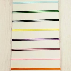 May include: A white card with 12 different colored cords, each with two parallel lines. The cords are red, black, blue, light blue, green, black, yellow, purple, maroon, pink, orange, silver, maroon, and black.