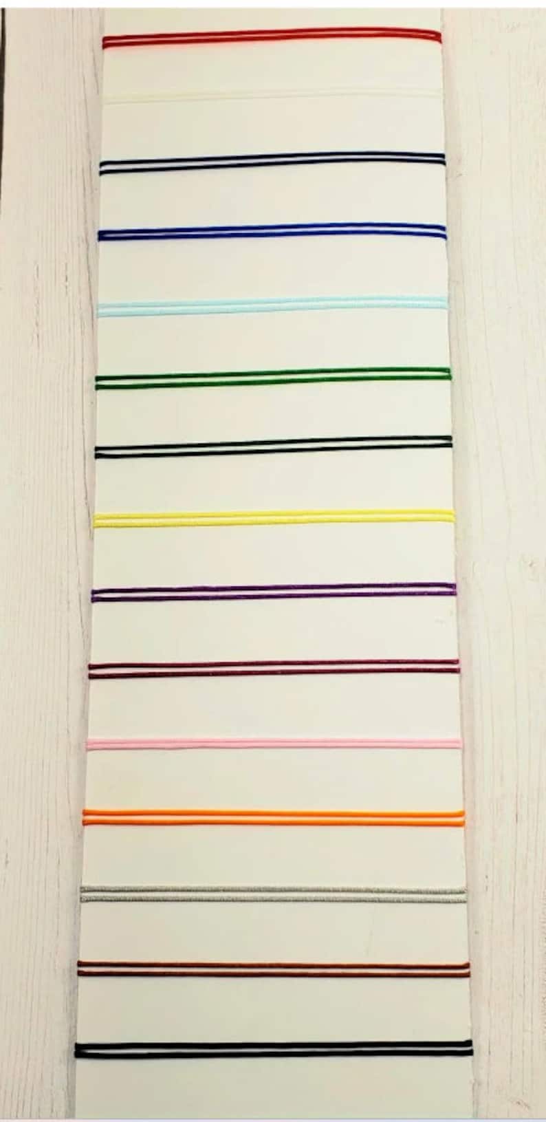 May include: A white card with 12 different colored cords, each with two parallel lines. The cords are red, black, blue, light blue, green, black, yellow, purple, maroon, pink, orange, silver, maroon, and black.