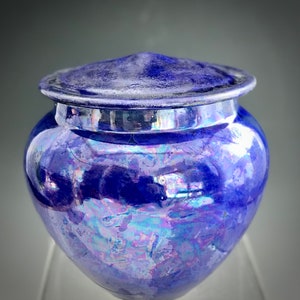 May include: A blue ceramic jar with a lid. The jar has a iridescent glaze with purple and pink hues.
