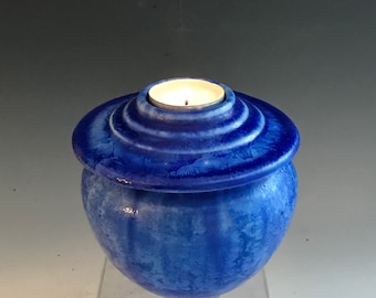 Könnte beinhalten: Eine blaue Keramikurne mit einem Deckel, auf dem sich ein kleiner Kerzenhalter befindet. Die Urne hat eine strukturierte, marmorierte Optik.