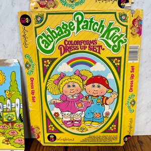 Può includere: Una scatola vintage Cabbage Patch Kids Colorforms Dress Up Set. La scatola gialla presenta il logo Cabbage Patch Kids e un'illustrazione colorata di due bambole. La scatola è leggermente usurata, mostrando la sua età.