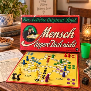 Könnte beinhalten: Ein Vintage-Brettspiel mit dem Titel Mensch ärgere Dich nicht in einer roten Schachtel mit einem spielenden Mann. Das gelbe Spielbrett enthält farbige Spielfiguren in Blau, Gelb, Lila, Grün und Rot sowie einen schwarzen Würfel und einen grünen Becher.