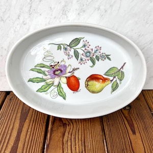 May include: An oval white ceramic serving platter featuring a botanical illustration. The design includes a purple and white passion flower, a small orange fruit, a green pear with brown speckles, and green leaves on thin brown stems.