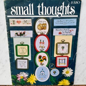 May include: A dark blue craft pattern booklet titled small thoughts featuring various cross-stitch designs including cats, a rooster, candles, a church, and floral motifs. The cover displays multiple finished embroidery projects in small frames.