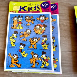 K&ouml;nnte beinhalten: Eine Packung mit vier Bl&auml;ttern Garfield Kids-Aufklebern. Die Aufkleber zeigen Garfield und Odie in verschiedenen Posen. Die Packung ist gelb und blau mit den Worten "Kids Stickers" und "99&cent; Ein super Preis!" bedruckt.