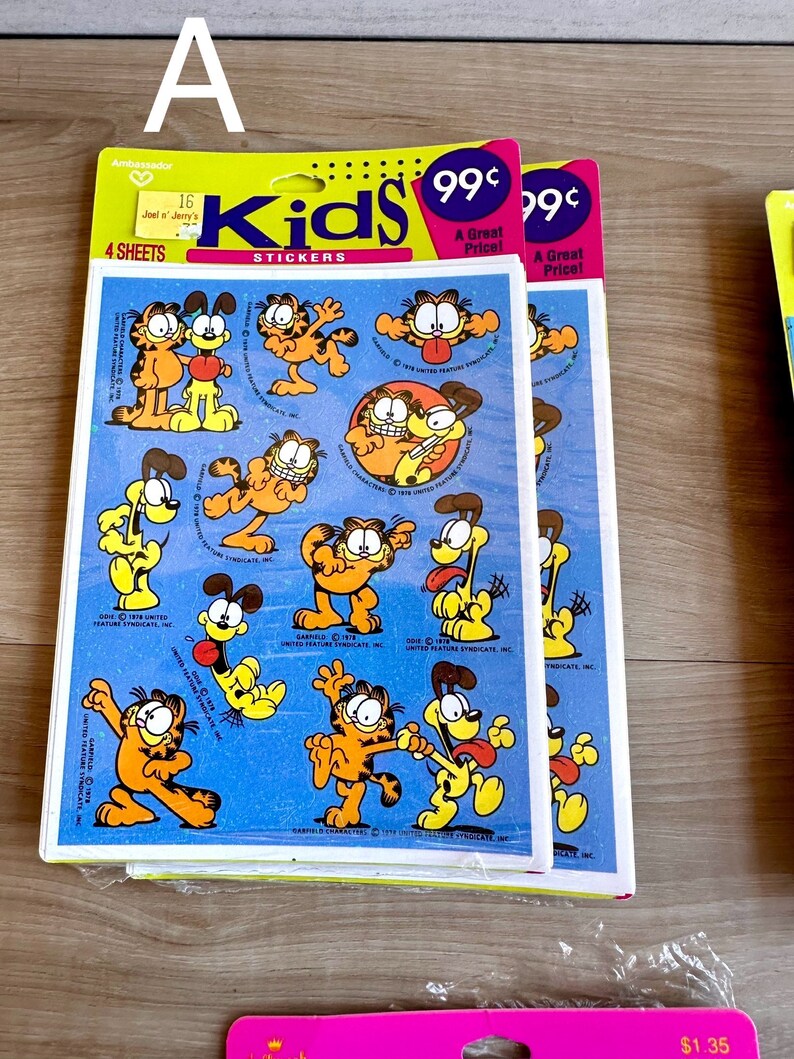 K&ouml;nnte beinhalten: Eine Packung mit vier Bl&auml;ttern Garfield Kids-Aufklebern. Die Aufkleber zeigen Garfield und Odie in verschiedenen Posen. Die Packung ist gelb und blau mit den Worten "Kids Stickers" und "99&cent; Ein super Preis!" bedruckt.