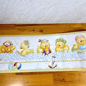 May include: A decorative border featuring five yellow cartoon ducks in a bubble bath. Each duck is wearing different accessories, such as goggles, a sailor hat, and a floral headpiece. A sailboat, soap, and a beach ball are also included.