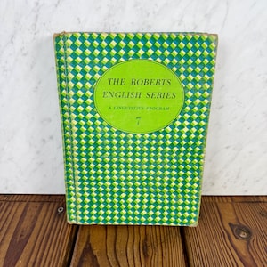 以下が含まれることがあります： 緑と白のチェック柄の「The Roberts English Series」というタイトルのヴィンテージ本。表紙にはタイトルと「A Linguistics Program」のテキストが入った緑色の円があります。数字の「7」が一番下にあります。