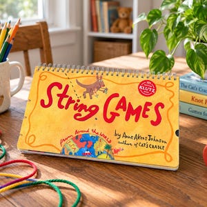 May include: A spiral-bound instructional book titled String Games from Around the World by Anne Akers Johnson. The yellow cover features a red kangaroo illustration, a globe graphic, and a red circular seal that reads 100% Certified Klutz Book.