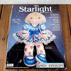 May include: A Starlight Doll Kit package by Daisy Kingdom featuring a printed fabric doll with blonde hair, blue and pink star-patterned clothing, and lace trim. The packaging includes text, style number 7202, and states the doll is 18 inches tall.