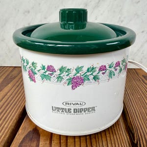 May include: A white Rival Little Dipper electric stoneware server with a green lid and rim. The server features a decorative grape vine pattern around the exterior. The text "Little Dipper" is printed on the front.