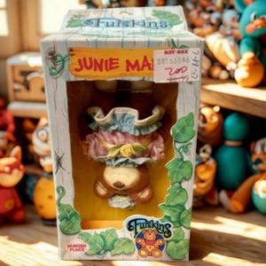 May include: A vintage "Furskins" Junie Ma bear doll in its original box. The box is decorated with green leaves and the bear is wearing a pink and blue dress. The box has a price tag from Kay-Bee.