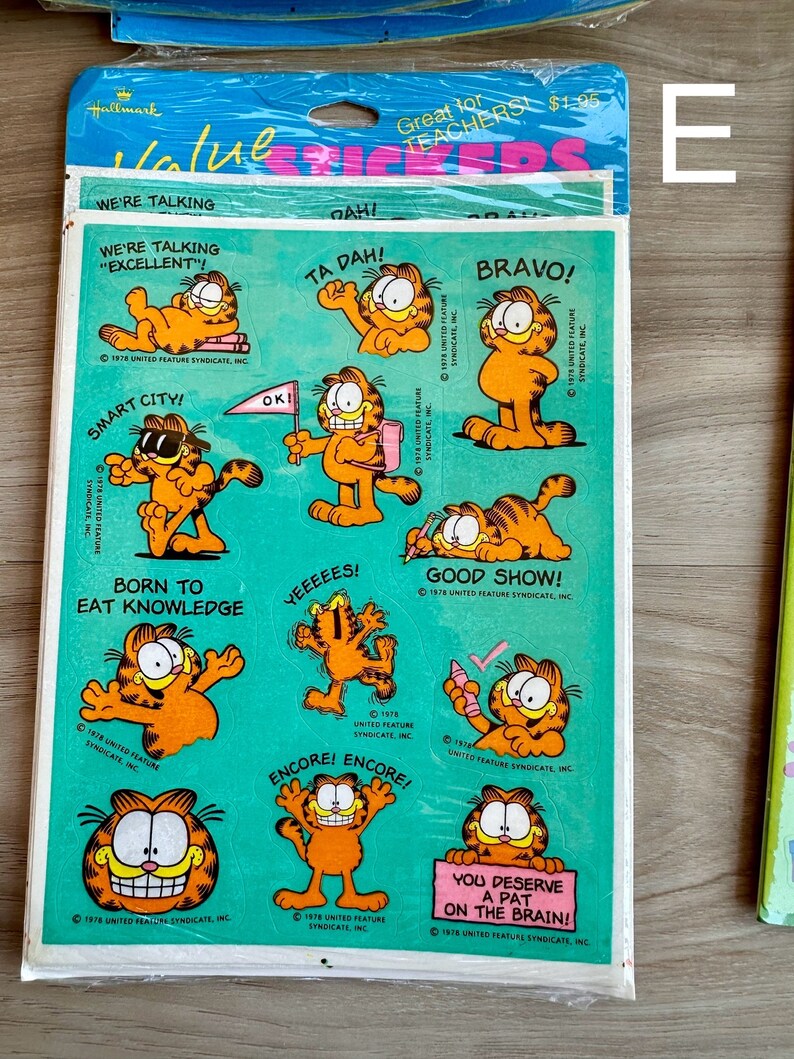 K&ouml;nnte beinhalten: Ein Bogen Garfield-Aufkleber mit verschiedenen Bildern der orangefarbenen Katze mit verschiedenen Spr&uuml;chen. Die Spr&uuml;che lauten: "Wir reden von 'exzellent'!", "Smart City!", "Geboren, um Wissen zu essen", "Ta Dah!", "Bravo!", "Yeeeeeees!", "Gute Show!", "Encore! Encore!" und "Du verdienst einen Klaps auf den Kopf!"