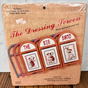 May include: A craft kit titled The Dressing Screen Three Screen Frame Set, featuring three arched wooden frames with white fabric inserts. Each insert displays a cross-stitched illustration of a goose playing a musical instrument: accordion, cello, and trumpet.