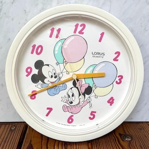 May include: White round Lorus Quartz clock featuring Mickey and Minnie Mouse holding balloons. The clock has pink numerals, a yellow second hand, and the text "©1984 The Walt Disney Company".
