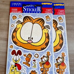 K&ouml;nnte beinhalten: Zwei Packungen Garfield-Aufkleberb&ouml;gen. Jede Packung enth&auml;lt zwei B&ouml;gen mit Aufklebern von Garfield und Odie. Die Aufkleber befinden sich auf einem blauen Hintergrund mit dem Text "Carlton Cards Sticker Station" und "Garfield" auf der Vorderseite.