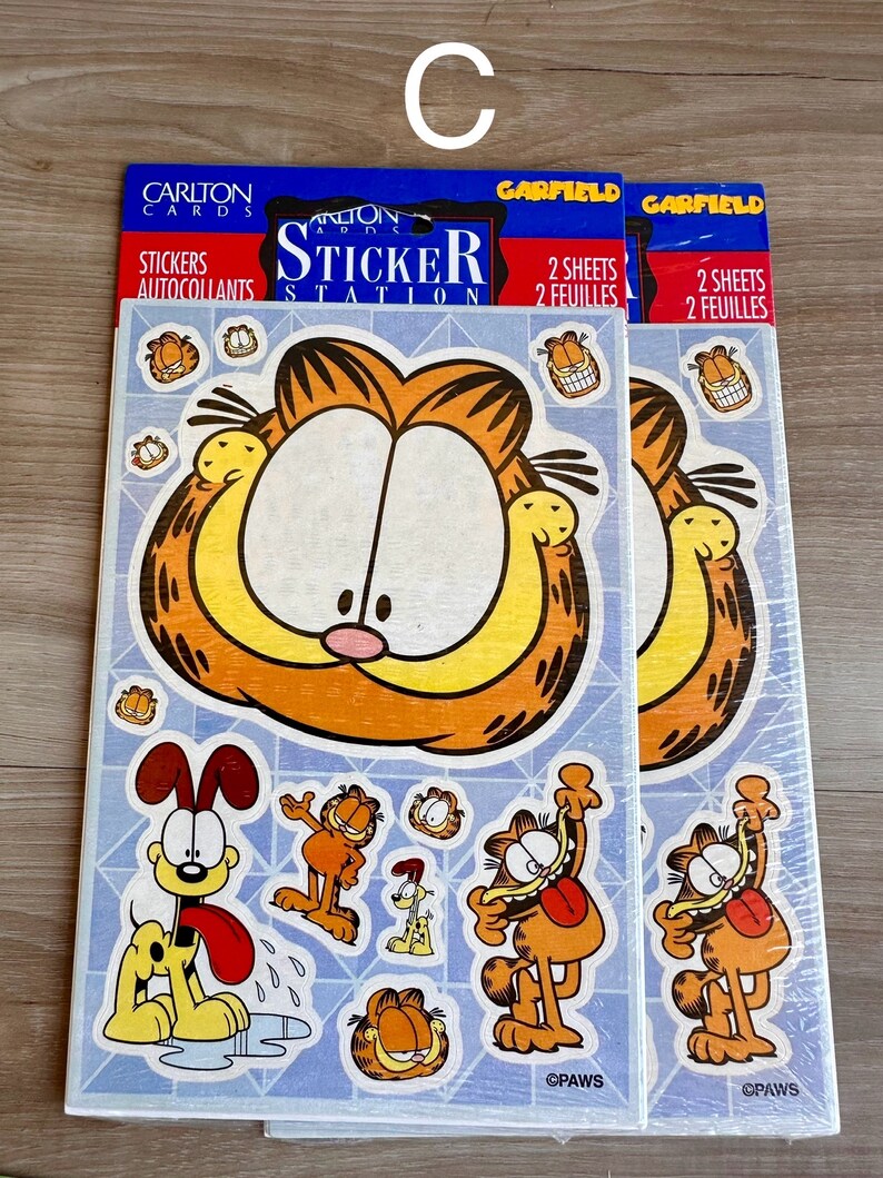 K&ouml;nnte beinhalten: Zwei Packungen Garfield-Aufkleberb&ouml;gen. Jede Packung enth&auml;lt zwei B&ouml;gen mit Aufklebern von Garfield und Odie. Die Aufkleber befinden sich auf einem blauen Hintergrund mit dem Text "Carlton Cards Sticker Station" und "Garfield" auf der Vorderseite.