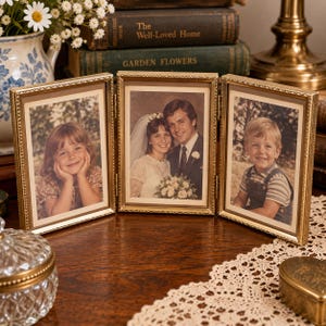 May include: A gold-toned metal triptych photo frame with a textured border, featuring three hinged panels. The left panel holds a photo of a young girl, the center a wedding couple, and the right a young boy, all displayed behind glass.