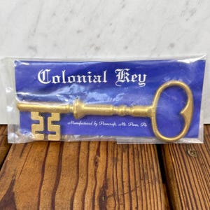 May include: A gold-colored Colonial Key in a clear plastic package. The key has a decorative design and the number 25 on the key's shaft. The package has the words "Colonial Key" in white script on a blue background.