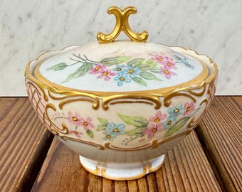 Bol de porcelana pintado a mano con tapa, firmado por Lou Powell en 1964, con borde dorado y detalles florales.