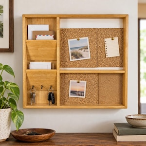 May include: A light-toned wooden wall organizer featuring two vertical mail slots on the left, three metal hooks for keys, and four cork board sections on the right. The cork boards display two square photographs and a small lined notepad paper.