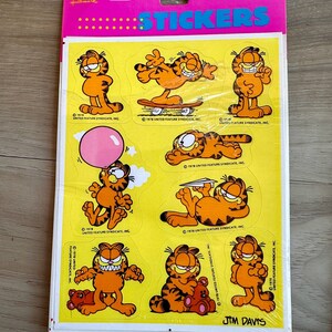 K&ouml;nnte beinhalten: Eine Bogen Garfield-Aufkleber mit dem orangefarbenen Tabby-Kater in verschiedenen Posen. Die Aufkleber befinden sich auf einem gelben Hintergrund mit dem Text "Stickers" und "Jim Davis", der auf dem Bogen gedruckt ist.