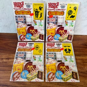 May include: Four Stencil Magic Country Collection packages featuring pre-cut reusable plastic stencils. Each card displays various craft projects like painted pillows, baskets, and boxes, with specific stencil designs including Santa, balloons, and colonial medallions.
