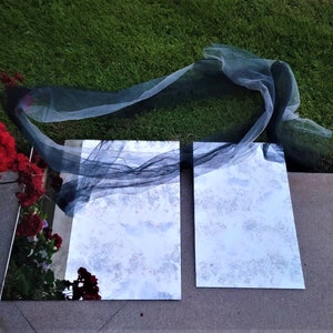 May include: Two rectangular mirrors with a black sheer fabric draped over them. The mirrors are sitting on a concrete surface with green grass in the background.