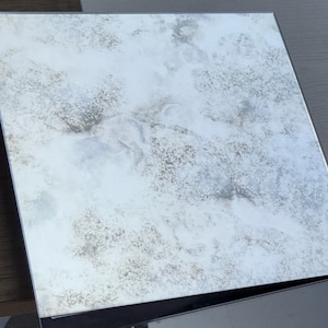 May include: A distressed silver mirror with a cloudy, textured surface. The mirror has a black frame.