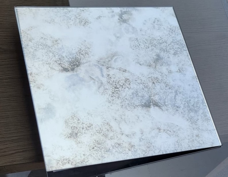May include: A distressed silver mirror with a cloudy, textured surface. The mirror has a black frame.