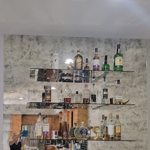 May include: A mirrored wall shelf with multiple glass shelves filled with various bottles of liquor. The bottles are arranged in rows and include brands like Jameson, Maker's Mark, and Patron.