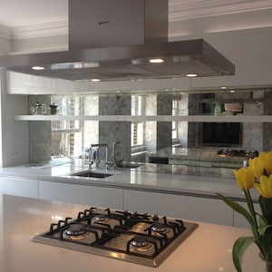 May include: A modern kitchen with white cabinets and a stainless steel range hood. The backsplash is made of mirrored tiles with a distressed finish. A bouquet of yellow tulips sits on the countertop.