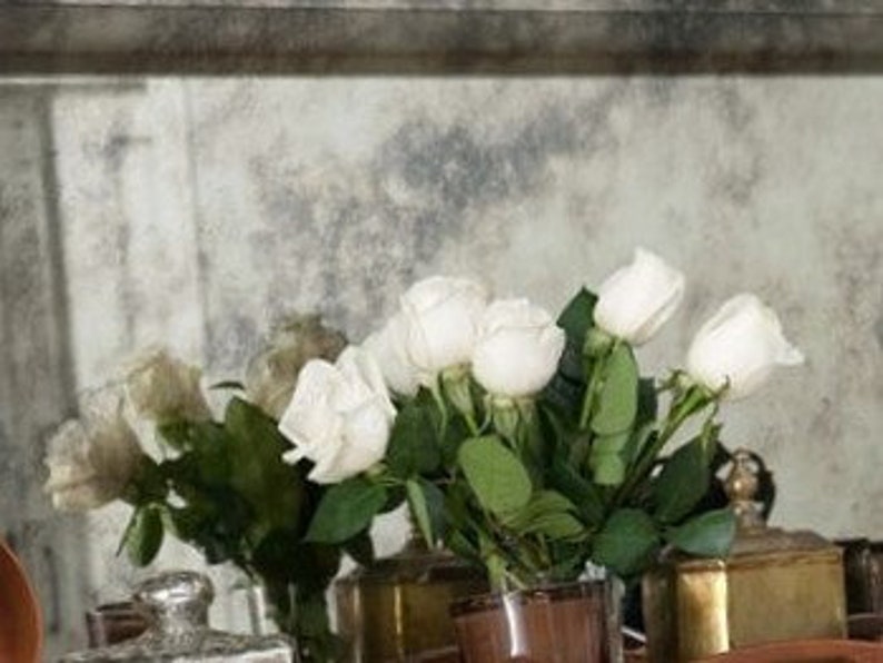 May include: A bouquet of white roses in a clear glass vase on a table with antique-looking silver and gold containers.