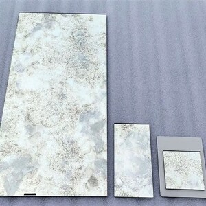 May include: Three rectangular pieces of glass with a white and grey mottled pattern. The largest piece is approximately 30 cm by 40 cm, the middle piece is approximately 15 cm by 20 cm, and the smallest piece is approximately 10 cm by 15 cm.