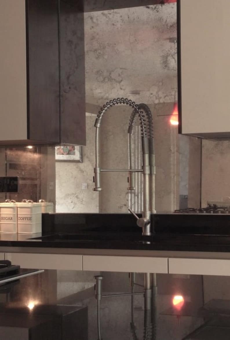 May include: A stainless steel kitchen faucet with a high arc spout and a pull-down sprayer. The faucet is mounted on a black countertop with a white cabinet below.