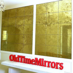 May include: Two large wall-mounted mirror panels composed of multiple square, gold-toned, antiqued glass tiles. In front of the mirrors, red three-dimensional lettering spells out the phrase OldTimeMirrors on a white ledge.