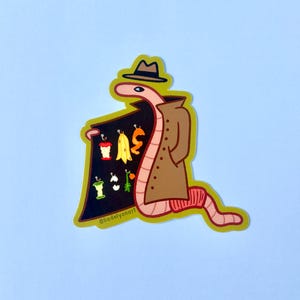 May include: A pink worm wearing a brown trench coat and a brown fedora hat, holding a black sign with the text "@liadelvonart" and various colorful fruits and vegetables on it.