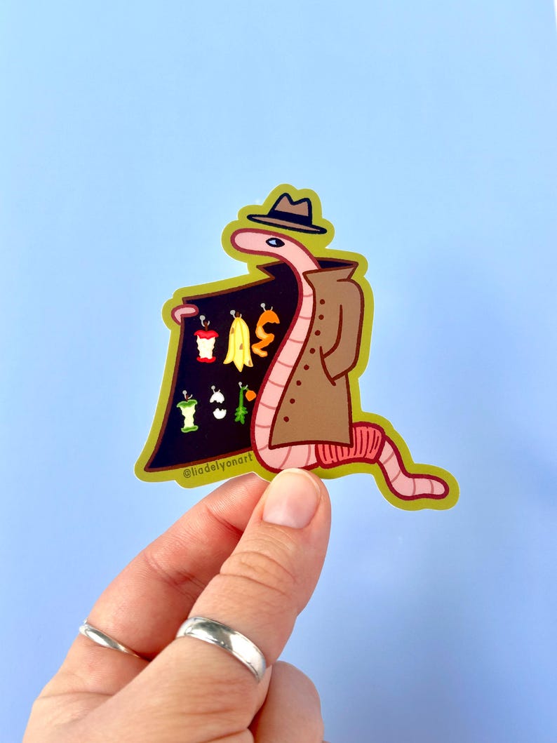 May include: A cartoon worm wearing a brown trench coat and a fedora holds a sign that says "I WAS", with a variety of fruit peels and cores on the sign. The worm is pink and yellow and has a black eye. The background is light blue.