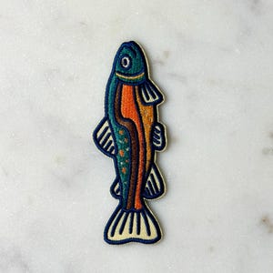 Pu&ograve; includere: Toppa ricamata a forma di pesce. Il pesce ha una testa turchese, un corpo arancione e dettagli blu e gialli. Adatto per abbigliamento o accessori.