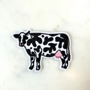 Op de afbeelding: Zwarte en witte geborduurde patch van een koe met een roze uier.