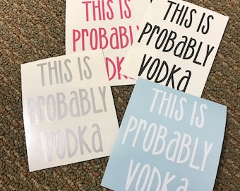 May include: Four white stickers with the text "This is probably vodka" in different colors and fonts. The stickers are on a brown carpet.