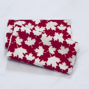 May include: Two red fabric squares with white maple leaf patterns. The fabric is folded in half.