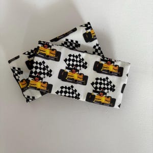 May include: Two white fabric pouches with a repeating pattern of yellow race cars and black and white checkered flags.