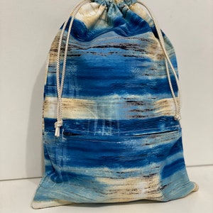 May include: A blue and beige drawstring bag with a white cord. The bag has a blue and beige abstract pattern that resembles waves. The bag has a small pocket on the front.