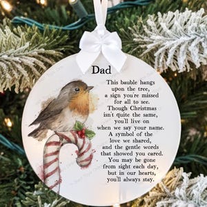 May include: A round Christmas bauble with a robin and candy cane design. The bauble has a white ribbon and bow. Text includes "Dad" and a poem about remembering a loved one during Christmas.