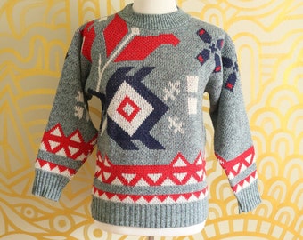 May include: A gray sweater with a geometric pattern in red, white, and blue. The sweater has a crew neck and long sleeves.