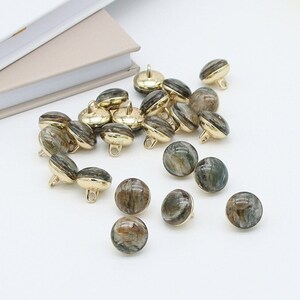 Op de afbeelding: Een verzameling van 18 ronde, bruine en groene knopen met gouden accenten. De knopen hebben een marmerpatroon en zijn perfect voor naaiprojecten.