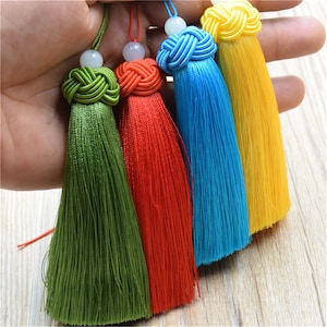 May include: Five colourful tassels with knotted tops and jade beads. The tassels are green, red, blue, and yellow.